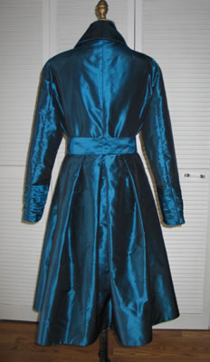 Back view features box pleating at waist and rouched cuffs at sleeves.